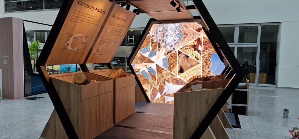 Hexagonale Holzkonstruktion eines Messestands mit eingebauten Stauraumfächern und LED-Installation
