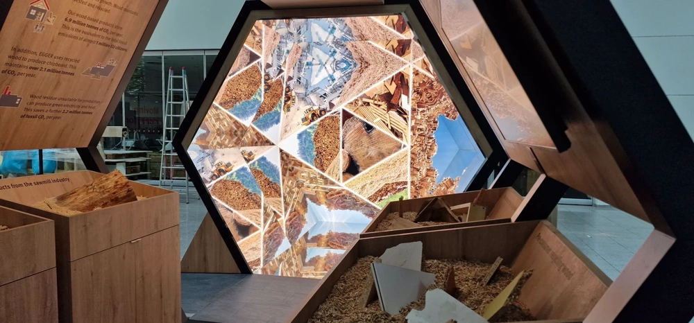 Messestand mit sechseckigen Displayrahmen und Holzspäne-Präsentationsmodulen