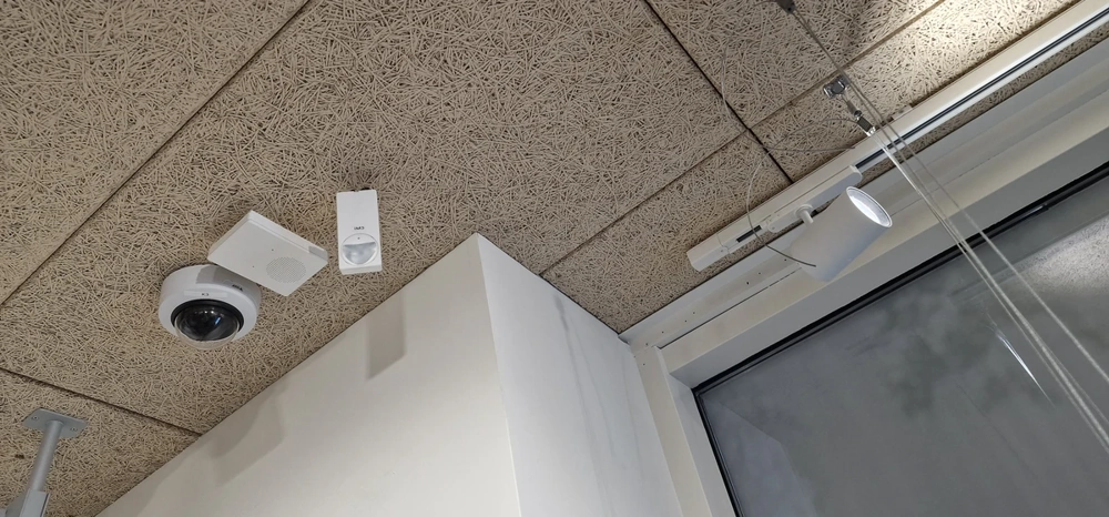 Ecke einer abgehängten Rasterdecke mit integrierter Kamera, Lautsprecher und Bewegungsmelder – Rasterdecke