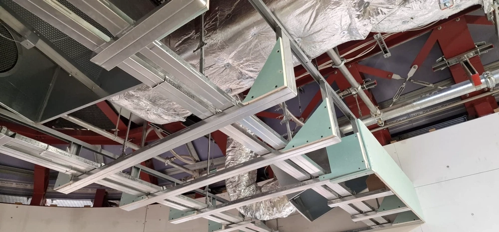 Montage einer Abgehängte decke mit Metallraster, Stahlunterkonstruktion und Lüftungsschläuchen im Rohbau