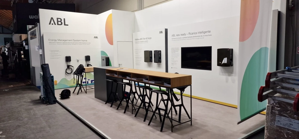 Messestandbau: weißer Messestand mit Bartheke, Hockern und Präsentationswänden