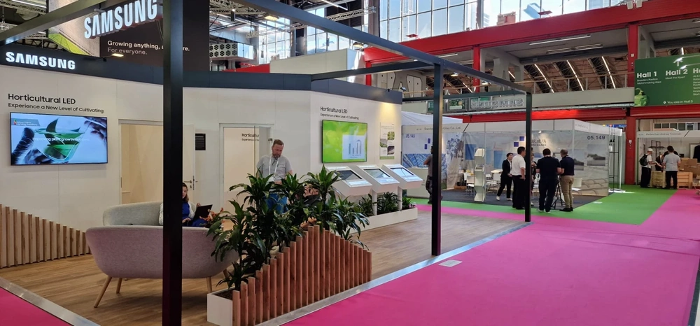 Messestandbau mit Pflanzenbegrenzung, interaktiven Touchscreens und moderner Lounge-Ecke auf hellem Messeboden