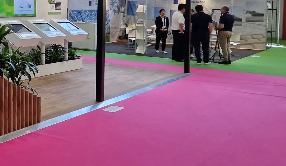 Offener Messestand mit pinkem Teppichboden, Infoterminals und vier Personen im Gespräch