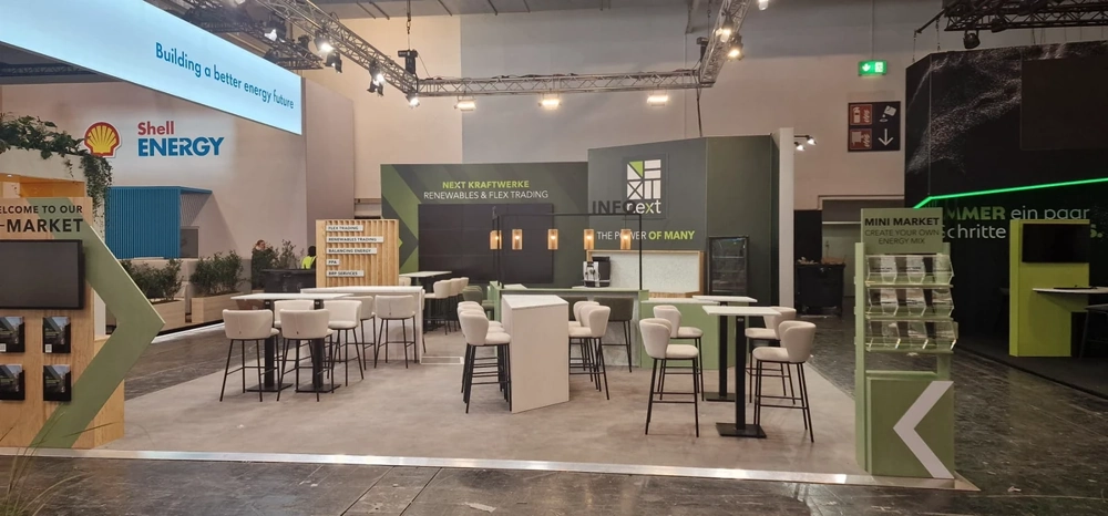 Modern gestalteter Messestand mit Stehtischen, Hockern und Theke auf grauem Boden