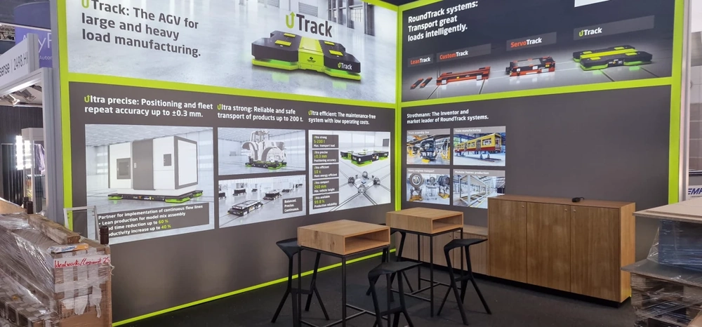 Zwei Hochtische, Barhocker und Sideboards vor beleuchteter Messestandwand im Aufbau – Eventmöbel montage