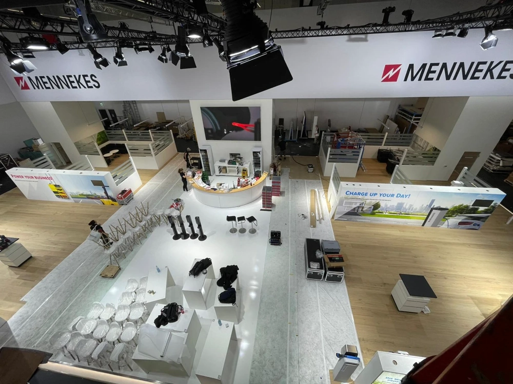 Messestandbau mit modularen weißen Wandelementen, Theke und Montage-Ausrüstung in offener Messehalle unter Deckenbeleuchtung