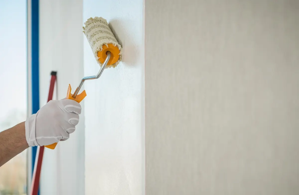 Hand mit weißem Handschuh streicht mit Farbrolle eine glatte weiße Wand – Malerarbeiten