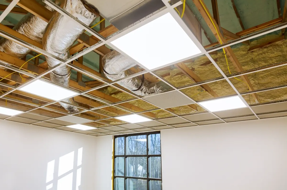 Abgehängte Rasterdecke mit sichtbarem Metallraster, Dämmmatten, integrierten LED-Lichtplatten und Lüftungsrohren