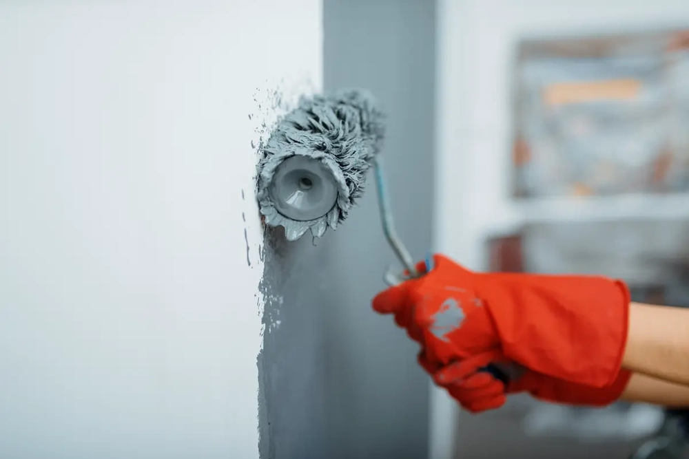 Hand streicht Wand mit Farbrolle bei Malerarbeiten im Innenausbau