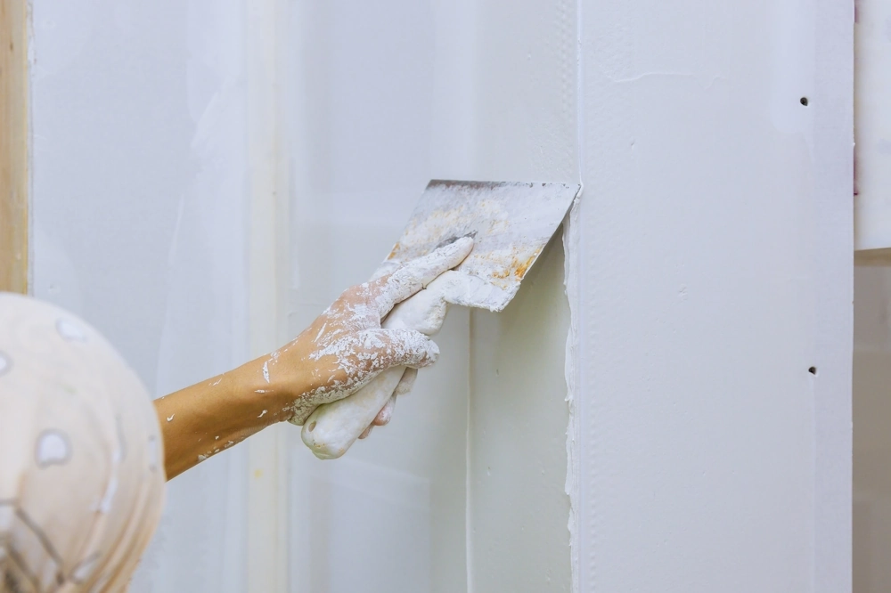 Hand mit Spachtel glättet Spachtelmasse bei Spachtelarbeiten an Trockenbauwand