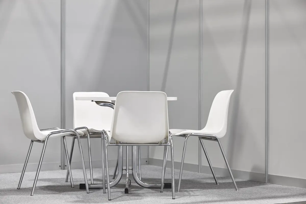 Vier weiße Stühle um einen runden Tisch auf grauem Teppich in Messestand – Eventmöbel montage