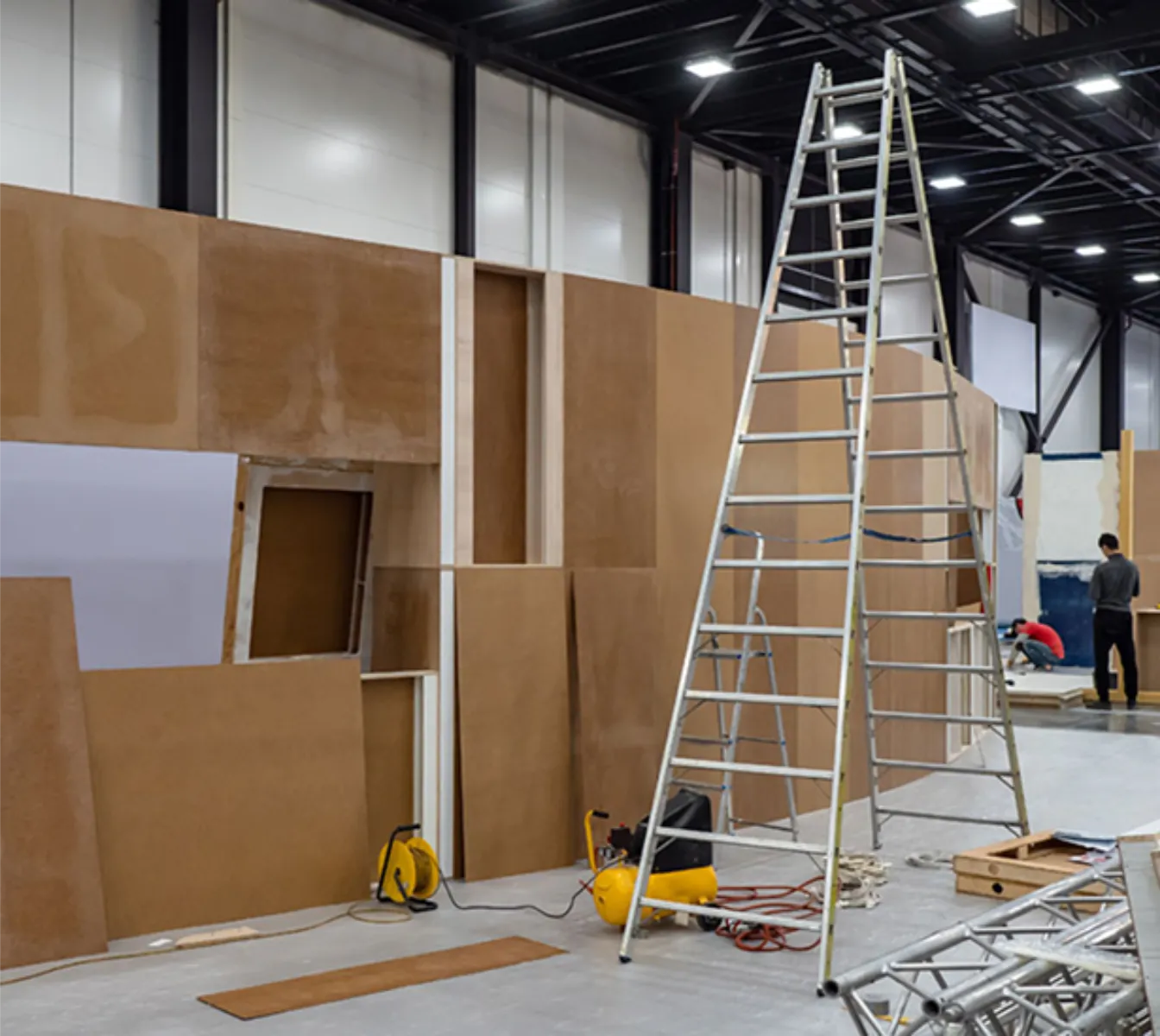 Montage von Holzwänden im Messestandbau mit Leitern, Kompressor und Bauequipment in Halle